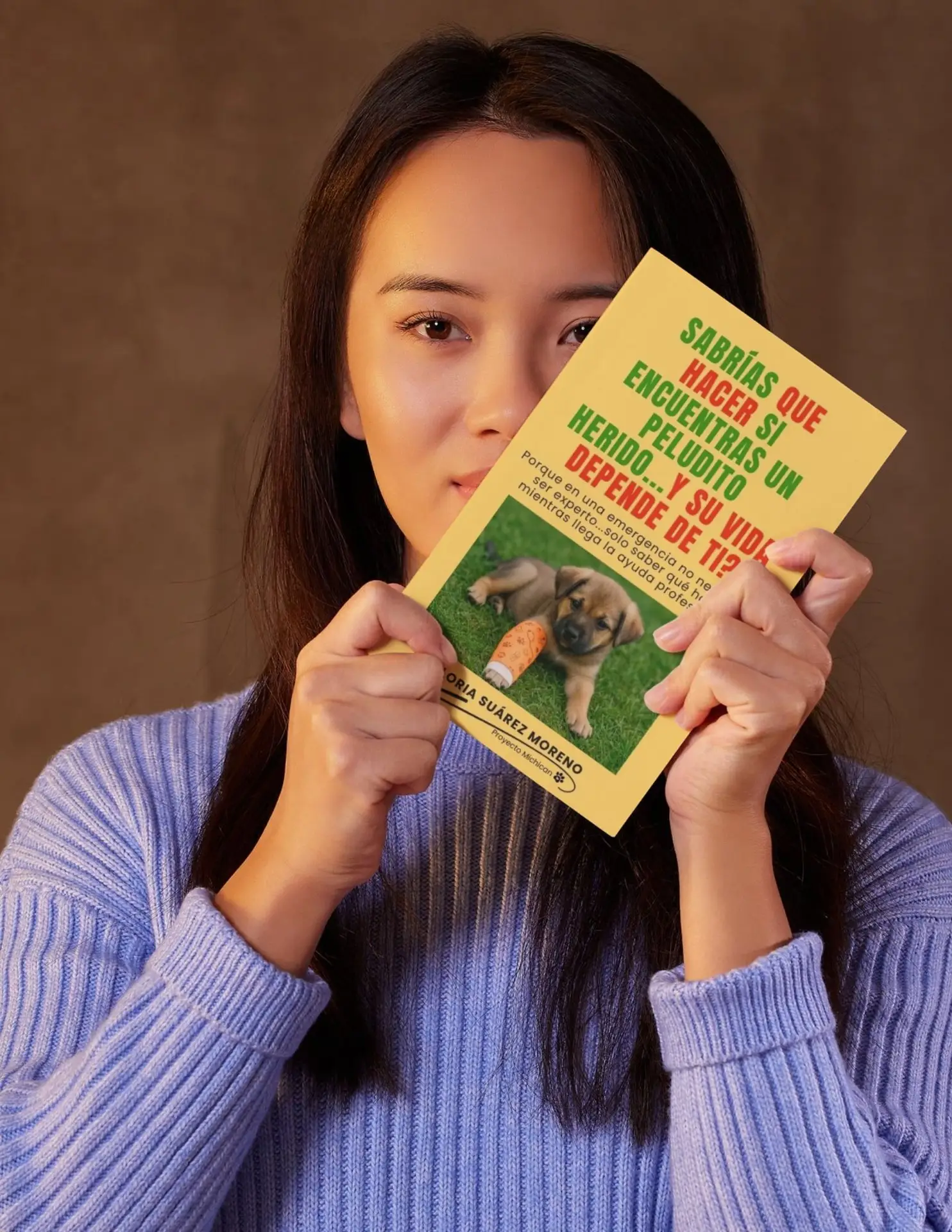 Mujer con suéter lila sosteniendo frente a su rostro la portada del ebook sobre qué hacer si encuentras un peludito herido.
